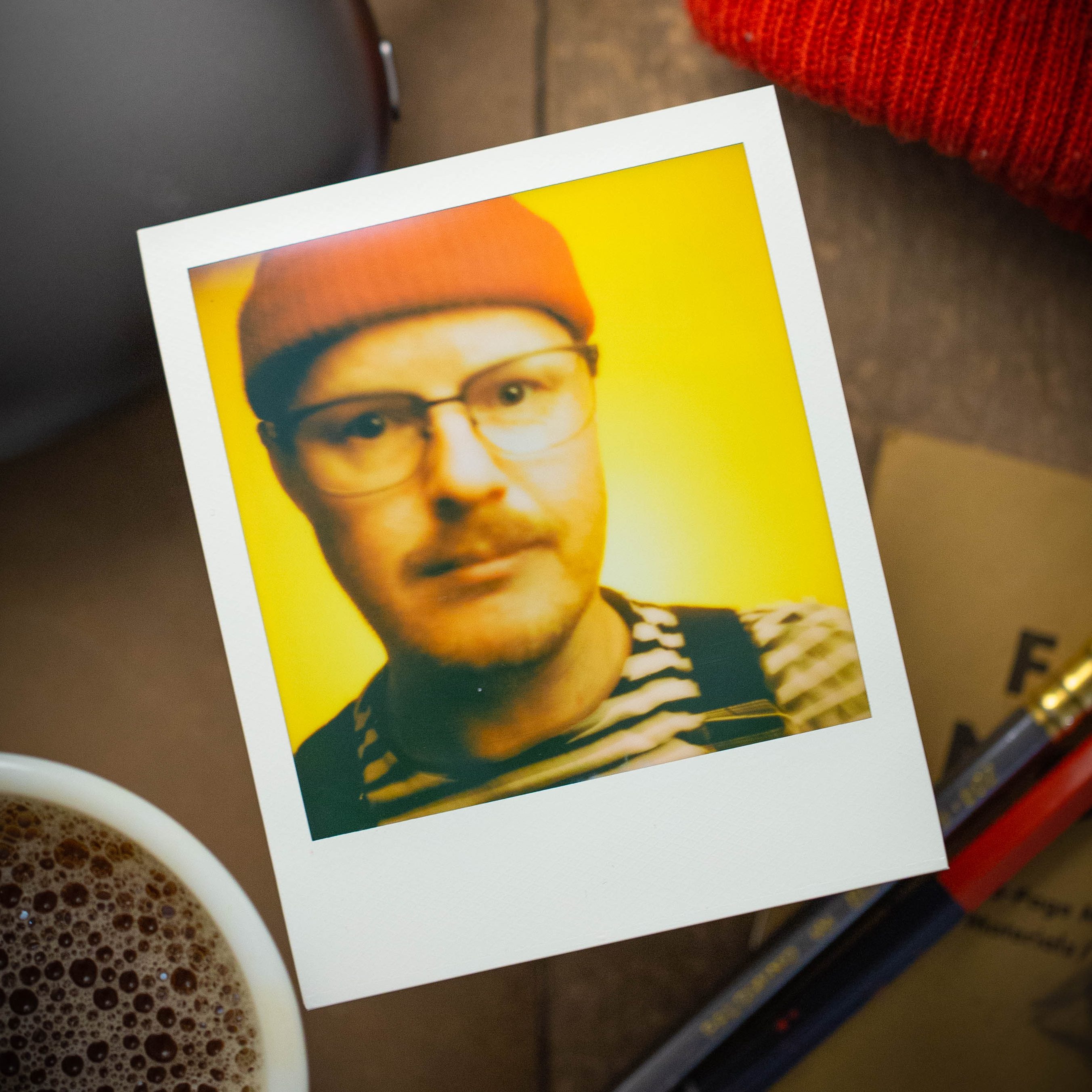 A POLAROID PORTRAIT OF A PERSON WEARING A RED CAP, OVERALLS, AND A STRIPED TEESHIRT.